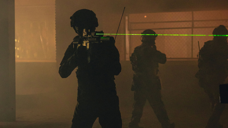 Armed tactical team in action at night using laser sights in an indoor setting.